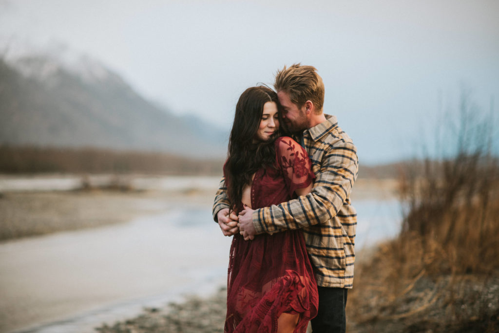 Couple hugging and laughing on an Alaska riverbed in front of the mountains