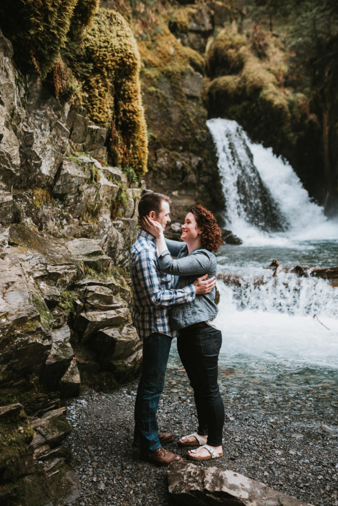 Couple standing looking at each other at base of waterfall