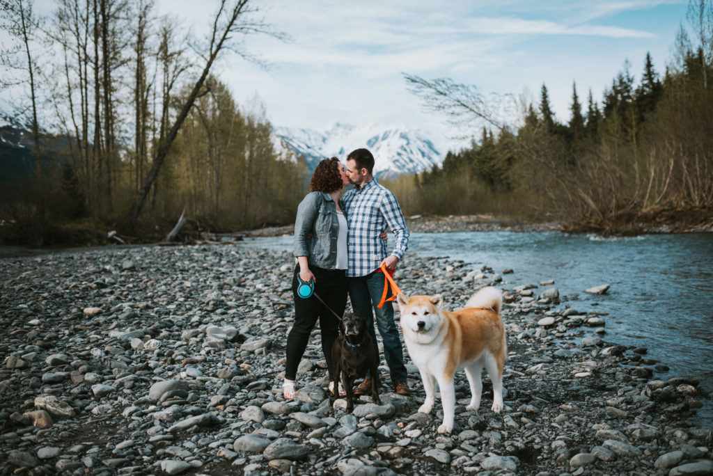 couple kissing while walking their dogs along riverbed