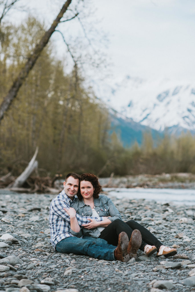 couple smiling at the camera while sitting on riverbed