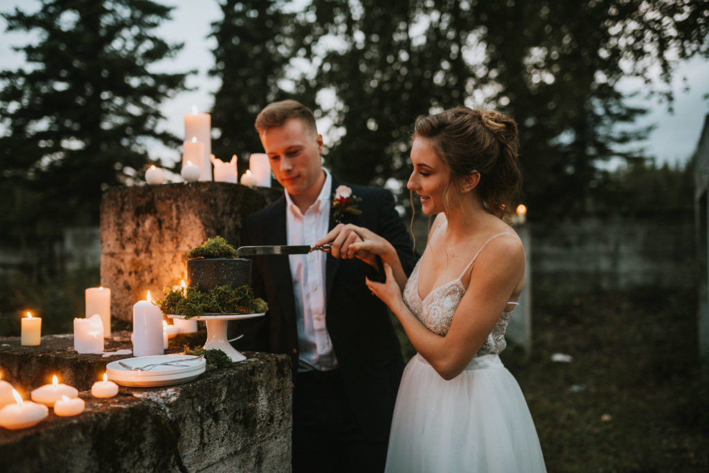Wedding couple cutting black cake with gold splatter and moss