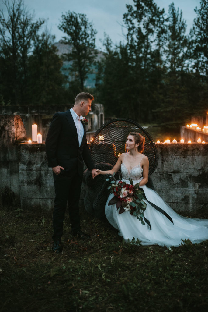 Bride and groom beside each other with black wicker chair and candlelight