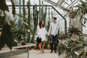Couple laughing standing side by side holding hands in greenhouse