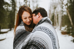 Couple snuggling with blanket in the woods