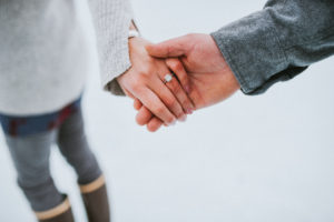 Couple holding hands to showcase engagement ring