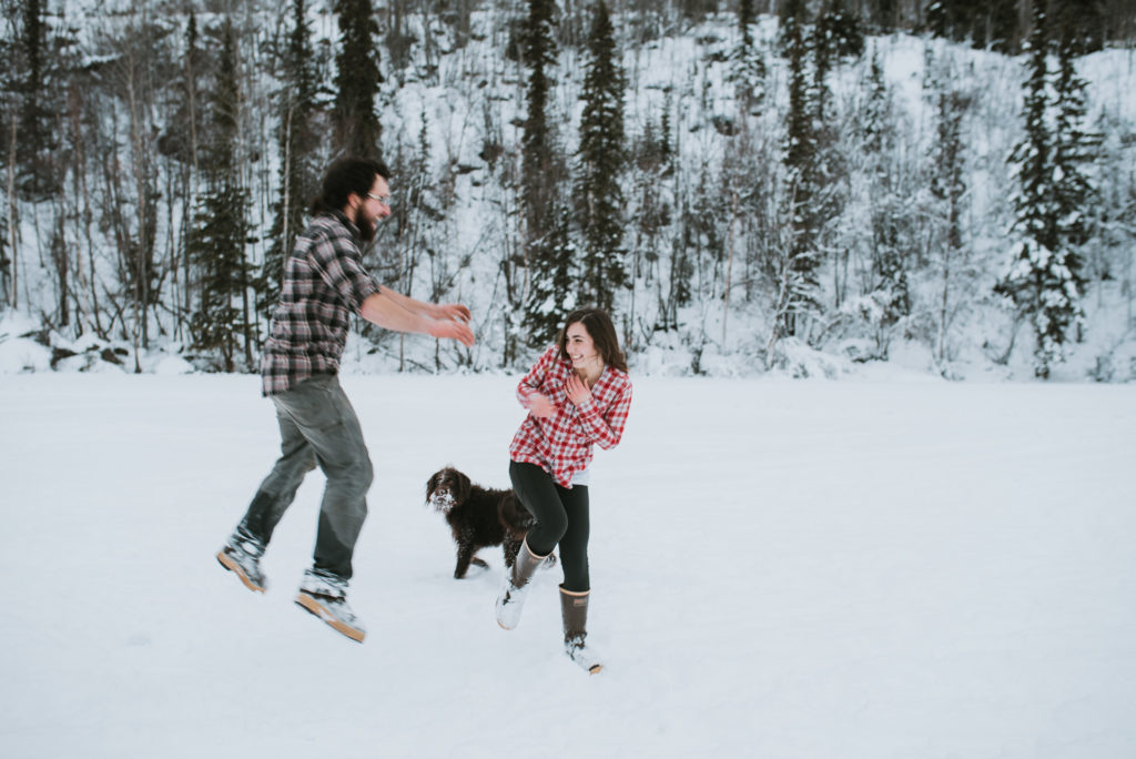 Couple playing with their dog in the snow during engagement session
