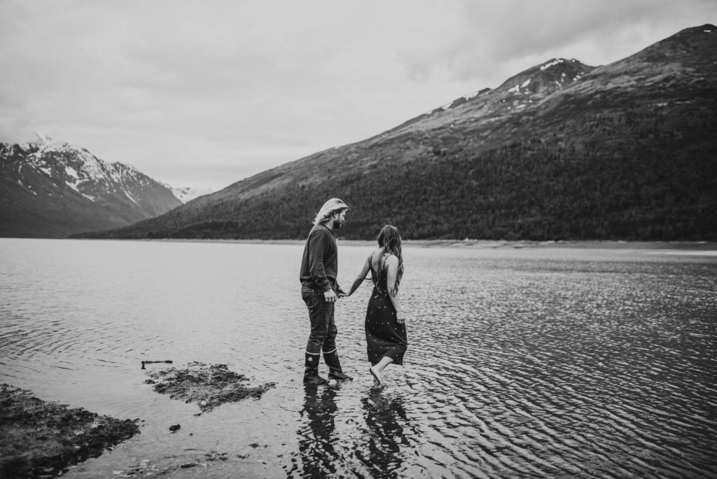 Black and white of couple walking into the lake holding hands