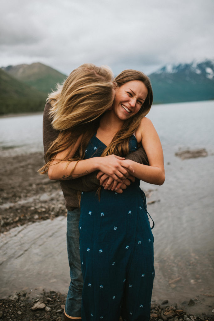 Couple hugging and laughing ona lake shore with mountain backdrop,
