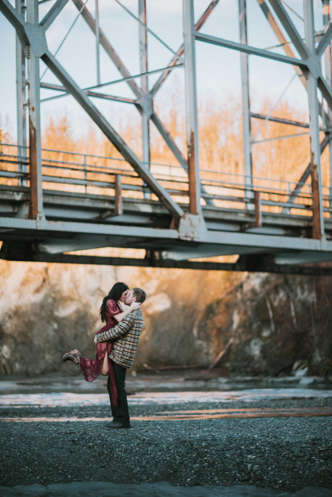 A couple standing under a bridge, girl is being picked up