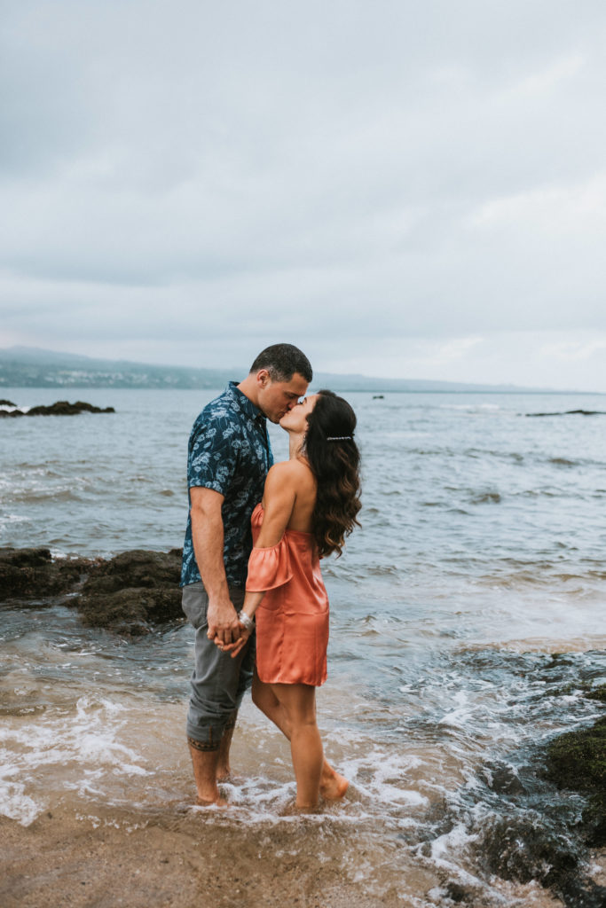 Couple standing in the water holding hands and kissing during hawaii engagement session