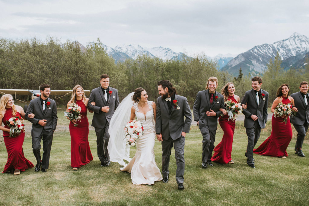 A wedding party with a mountain back drop, girls in maroon dresses and guys in grey tuxes