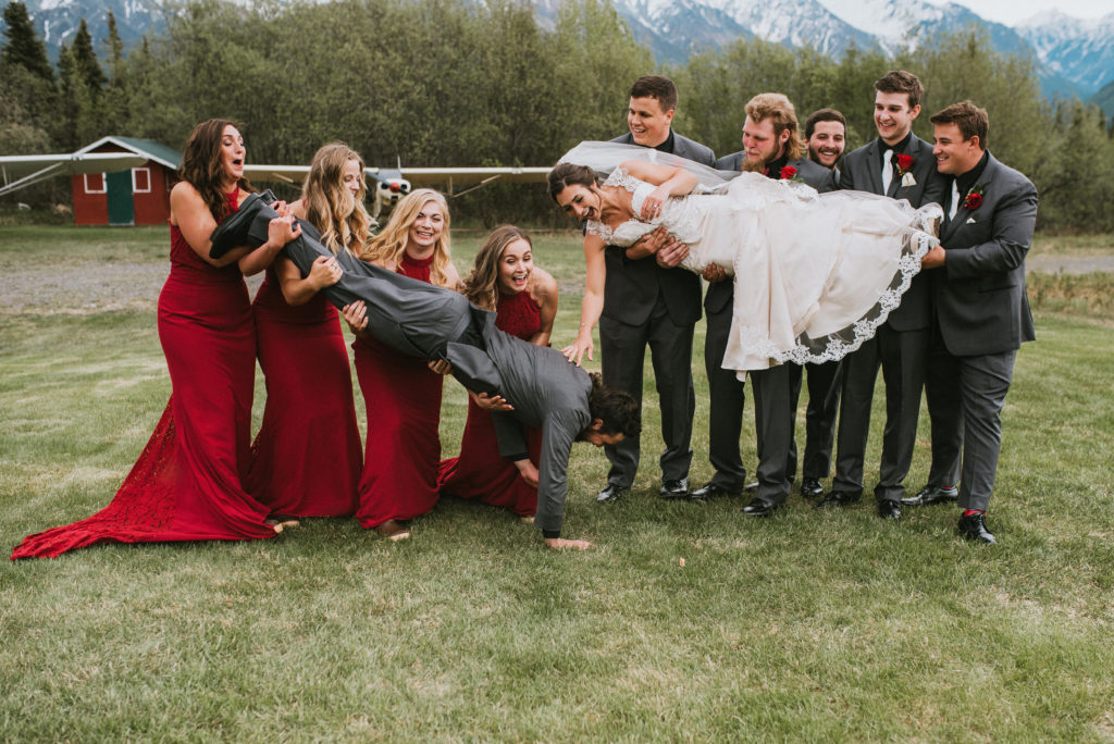 A wedding party with a mountain back drop, girls in maroon dresses and guys in grey tuxes