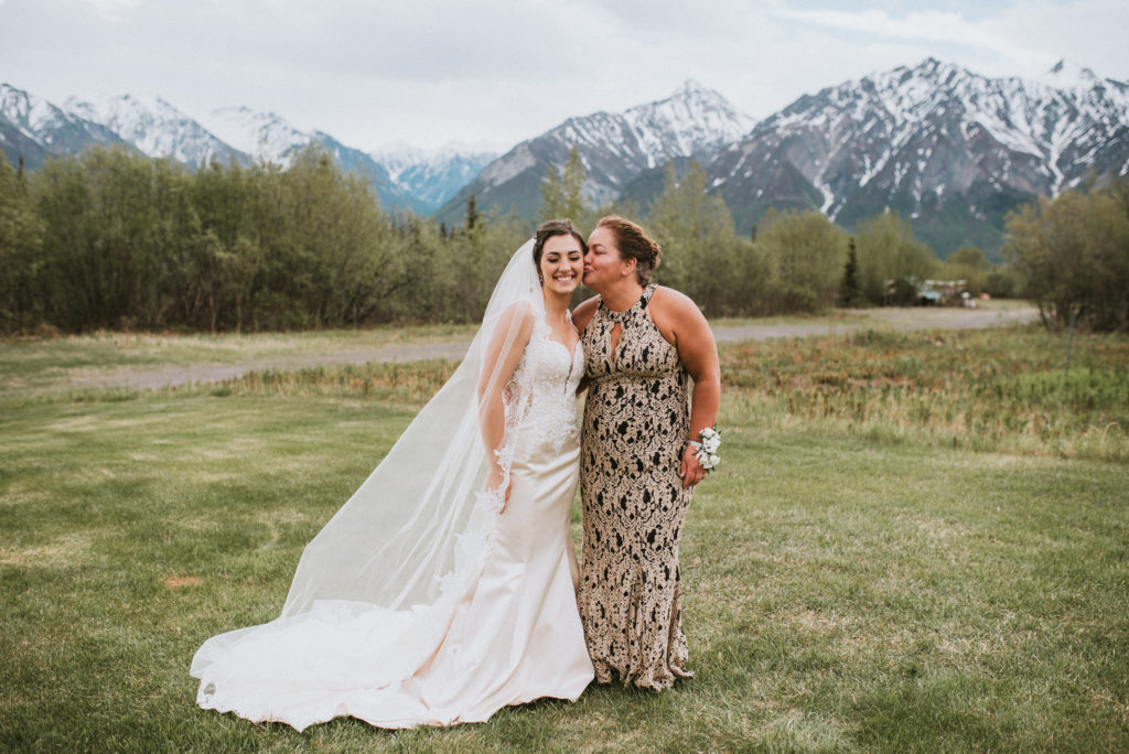 Bride with Mom kissing cheek, mountain backdrop