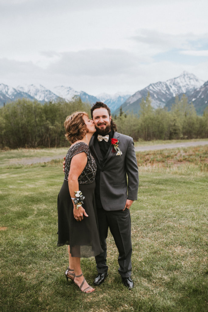 Groom with mom kissing his cheek with mountain backdrop