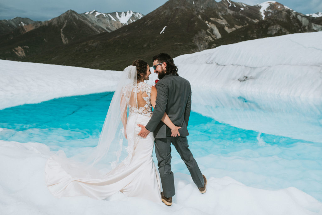 bride and groom on a glacier with blue water and mountains
