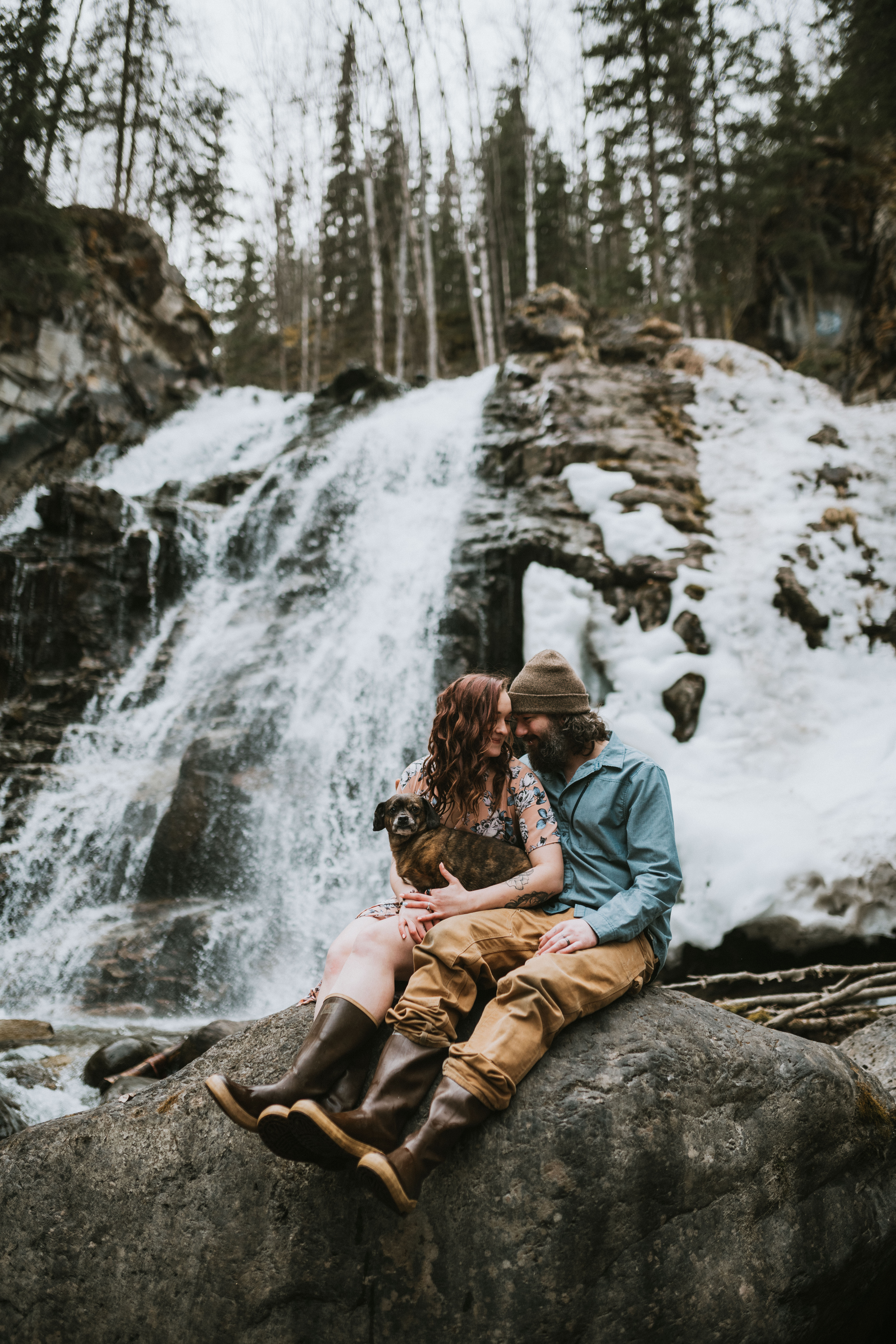 Couple sitting on a rock in front of a waterfall with their dog