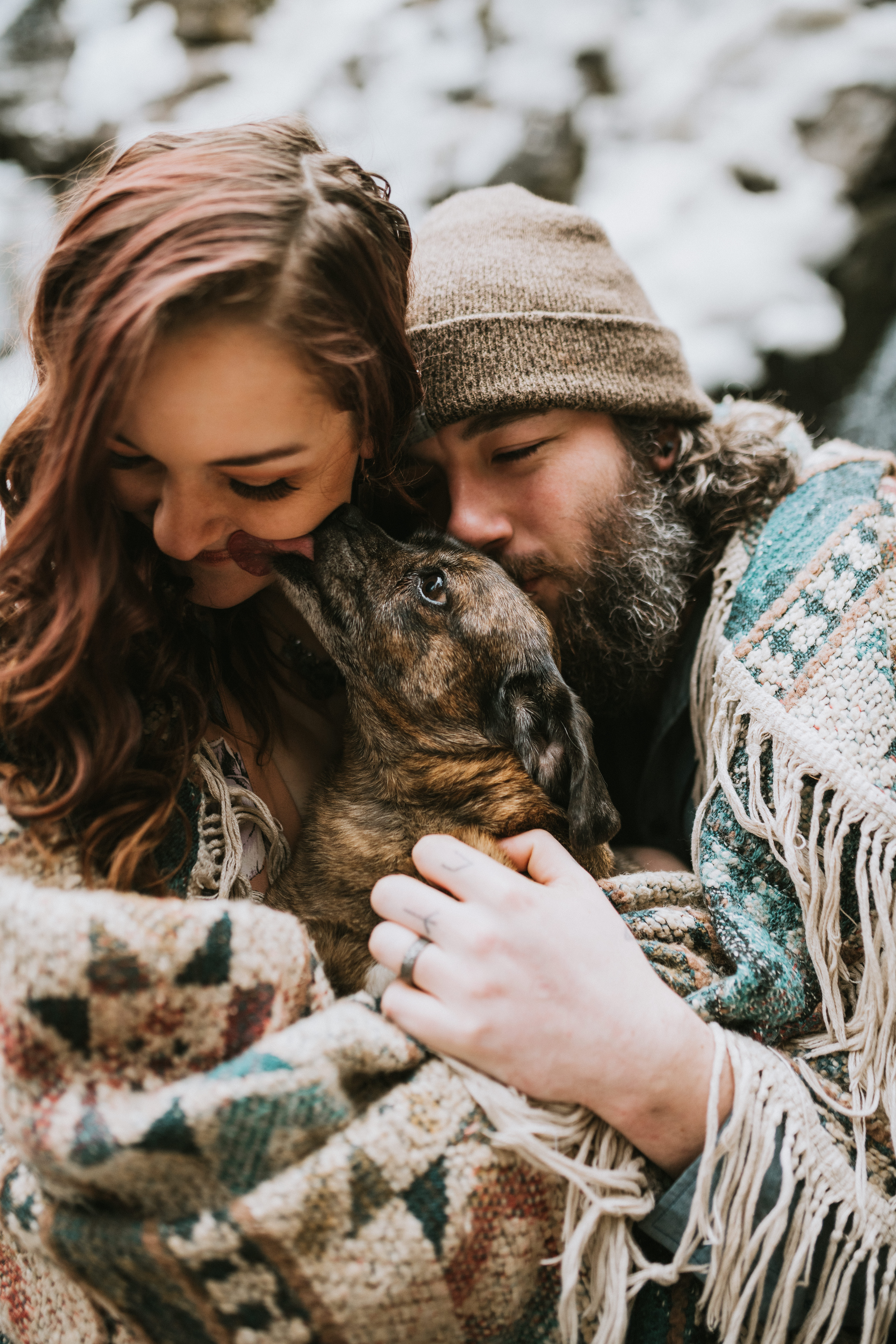 Couple with their dog wrapped in a blanket snuggling in front of a waterfall