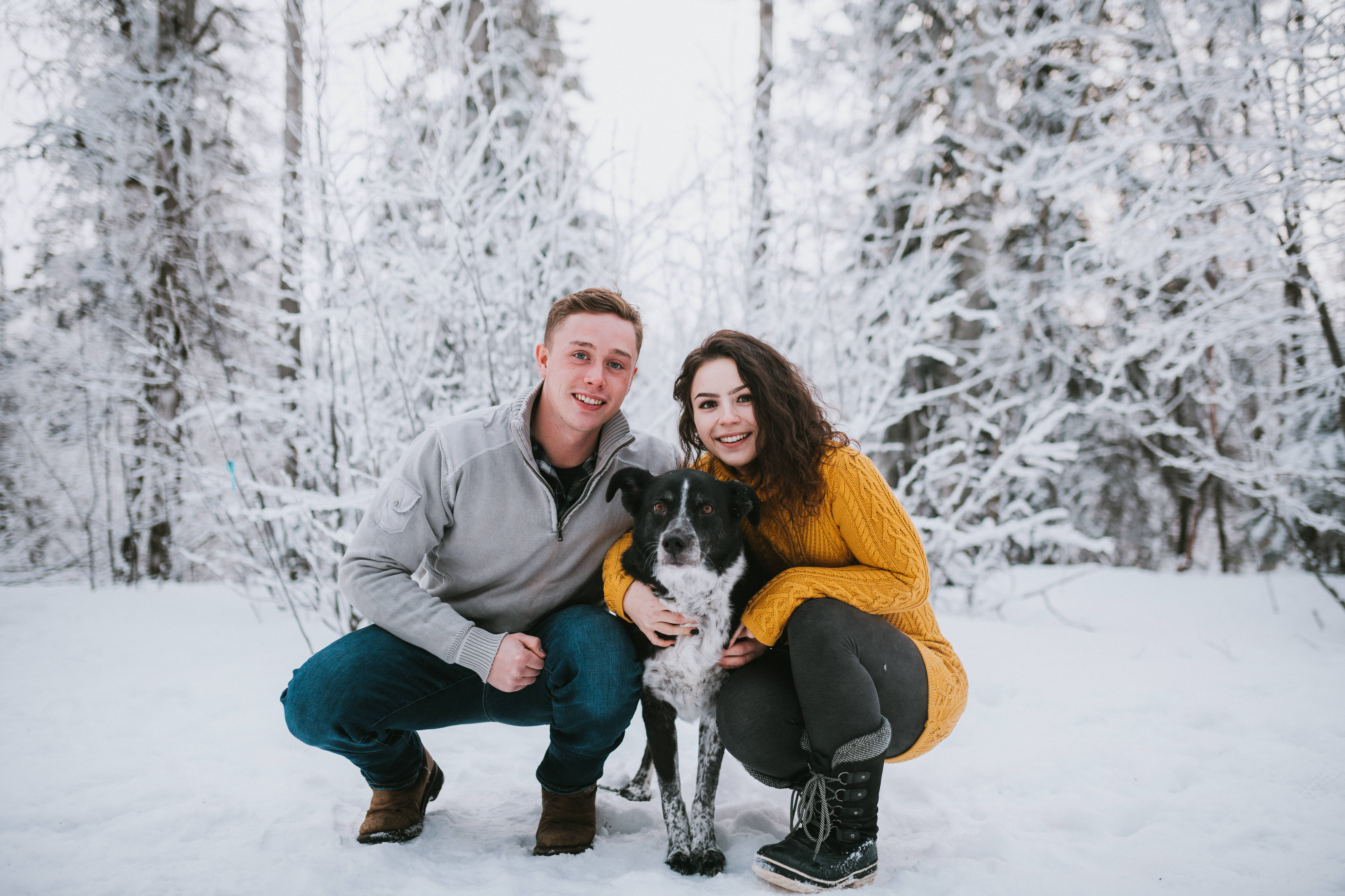 Couple crouching in snow with their dog during engagement session
