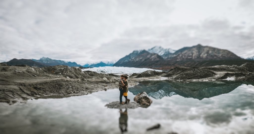 Wide panorama photo of a couple standing in the middle of a Glacier lake at Matanuska Glacier Park.