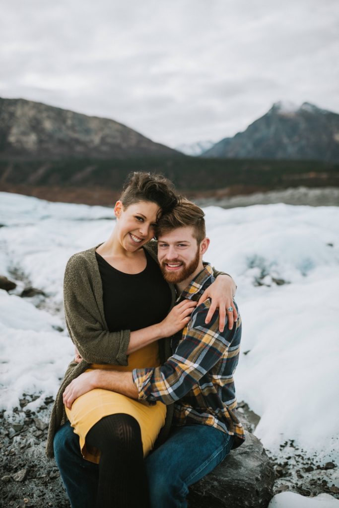 A couple snuggling and smiling at the camera during their fun engagement session.
