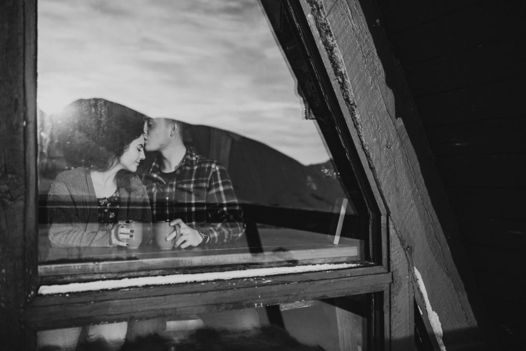 Couple where boy is kissing girl on the forehead in Hatcher Pass Lodge, looking in through the window