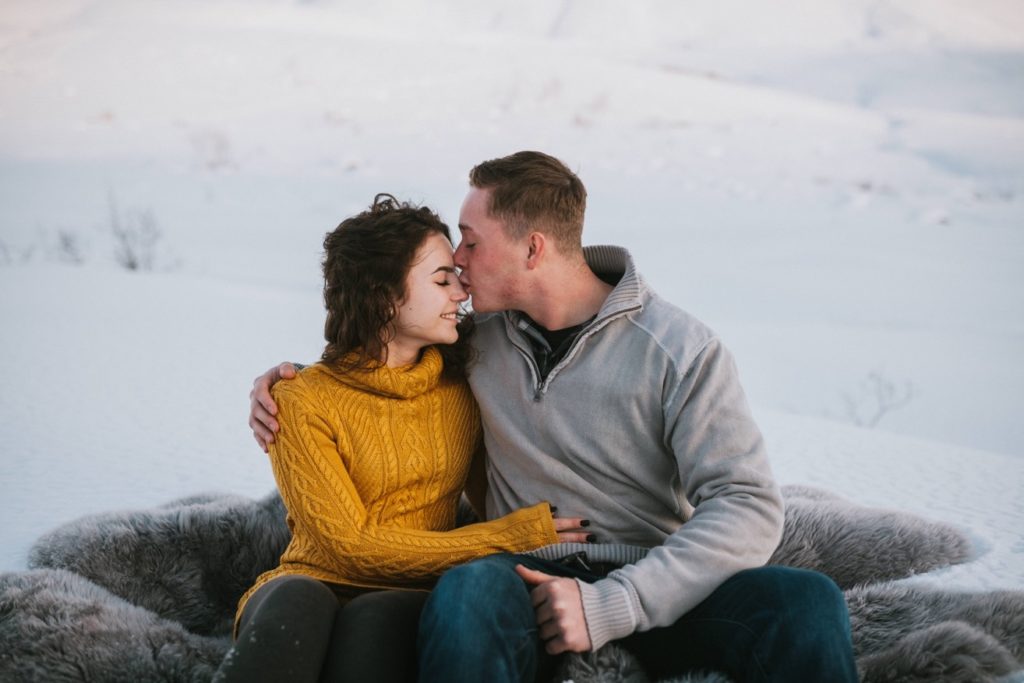 Couple snuggling during their Hatcher Pass engagement session while sitting in the snow