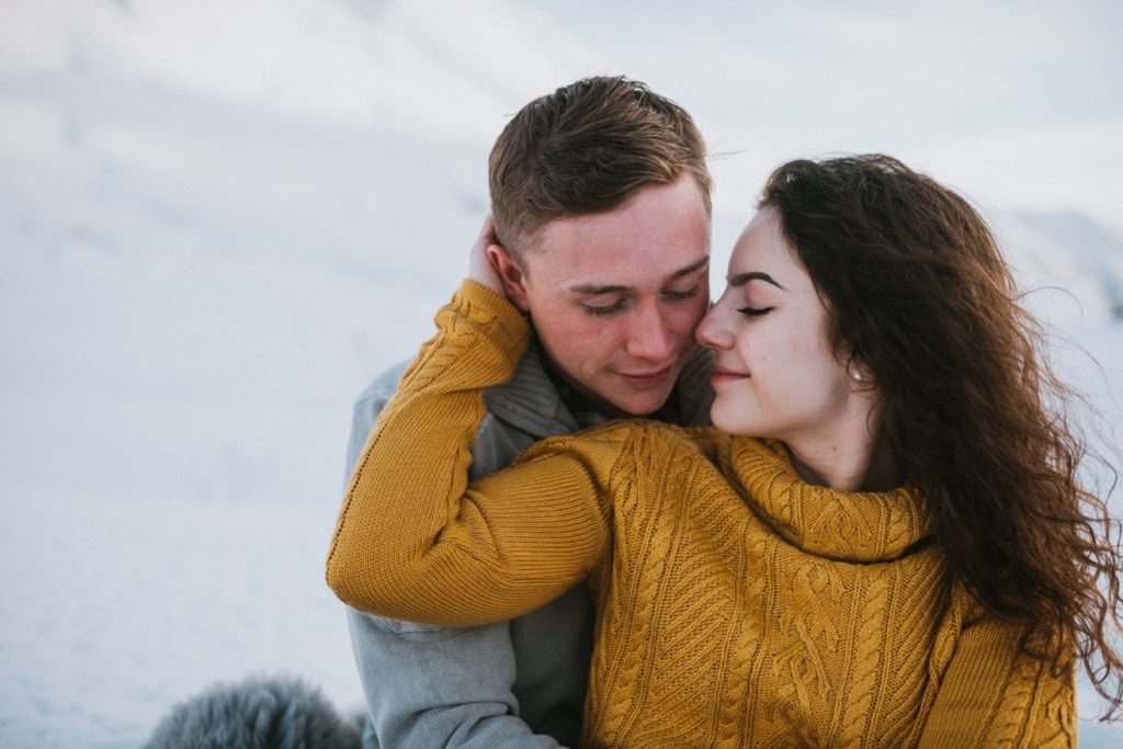 Couple snuggling during their Hatcher Pass engagement session while sitting in the snow