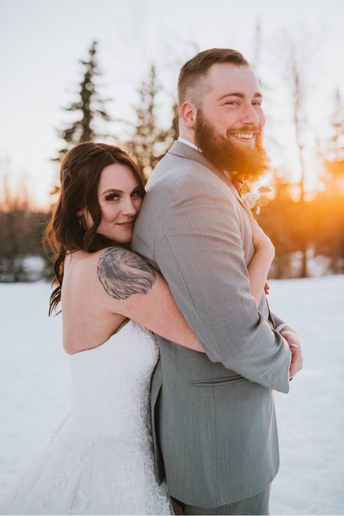 Bride hugging groom in sunset light during Alaska winter wedding