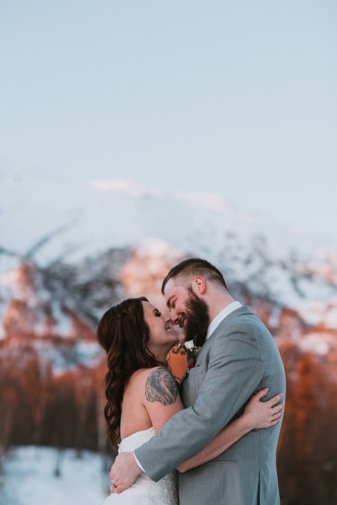 Bride and groom almost kissing in sunlight in front of mountains