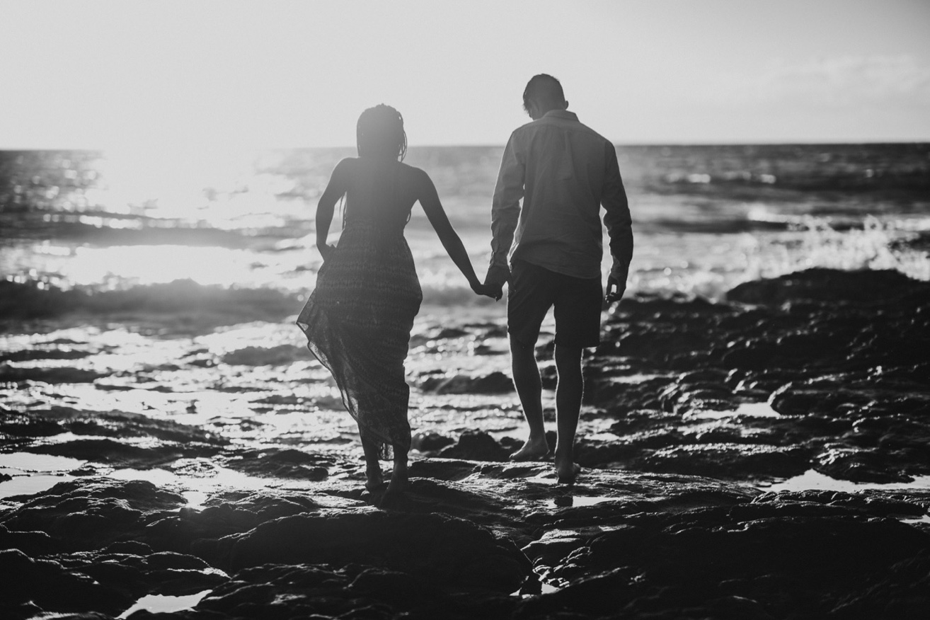 black and white photo of a couple walking into the sunset on a beach