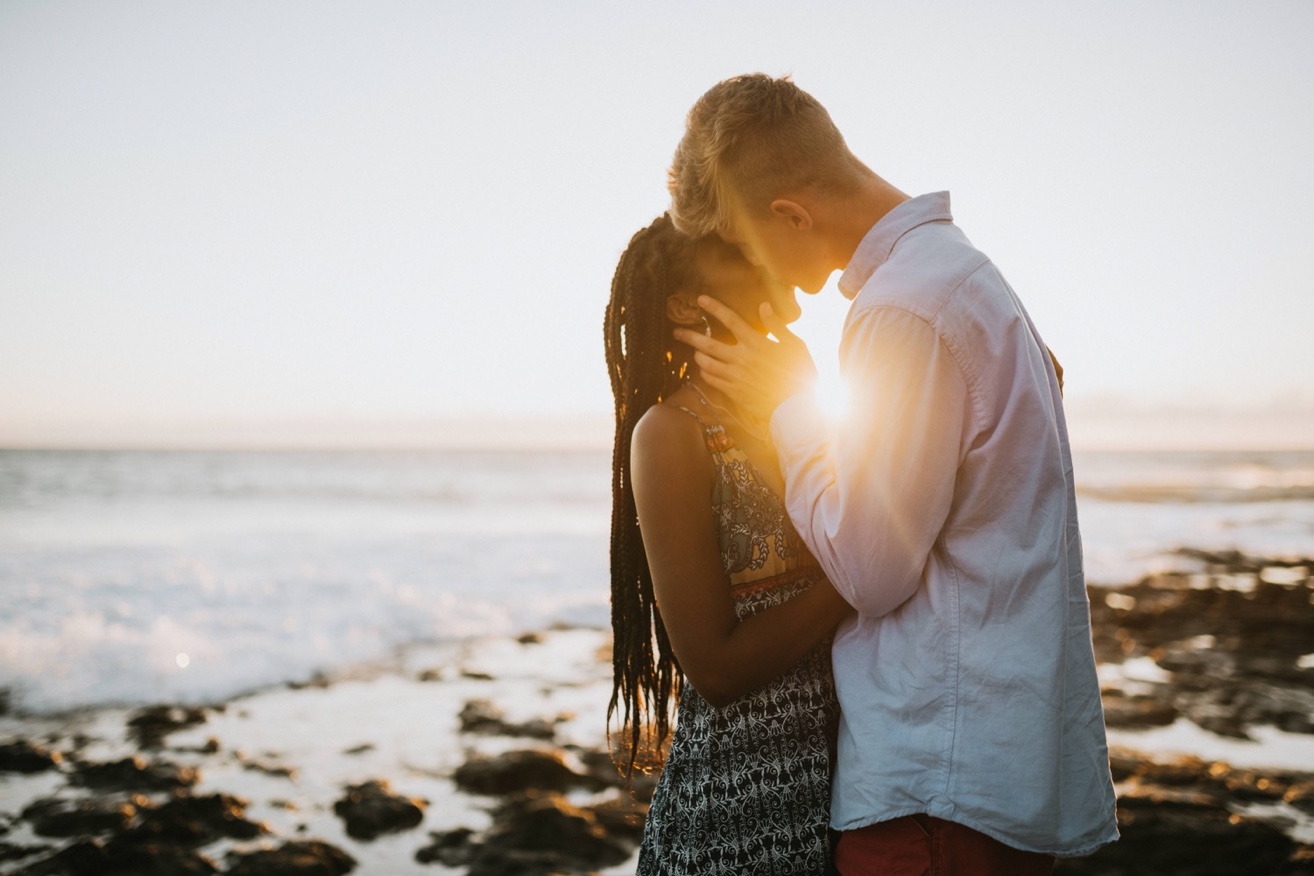 Couple kissing on the beach with a sunset shining between them during their engagement session with a kona photographer