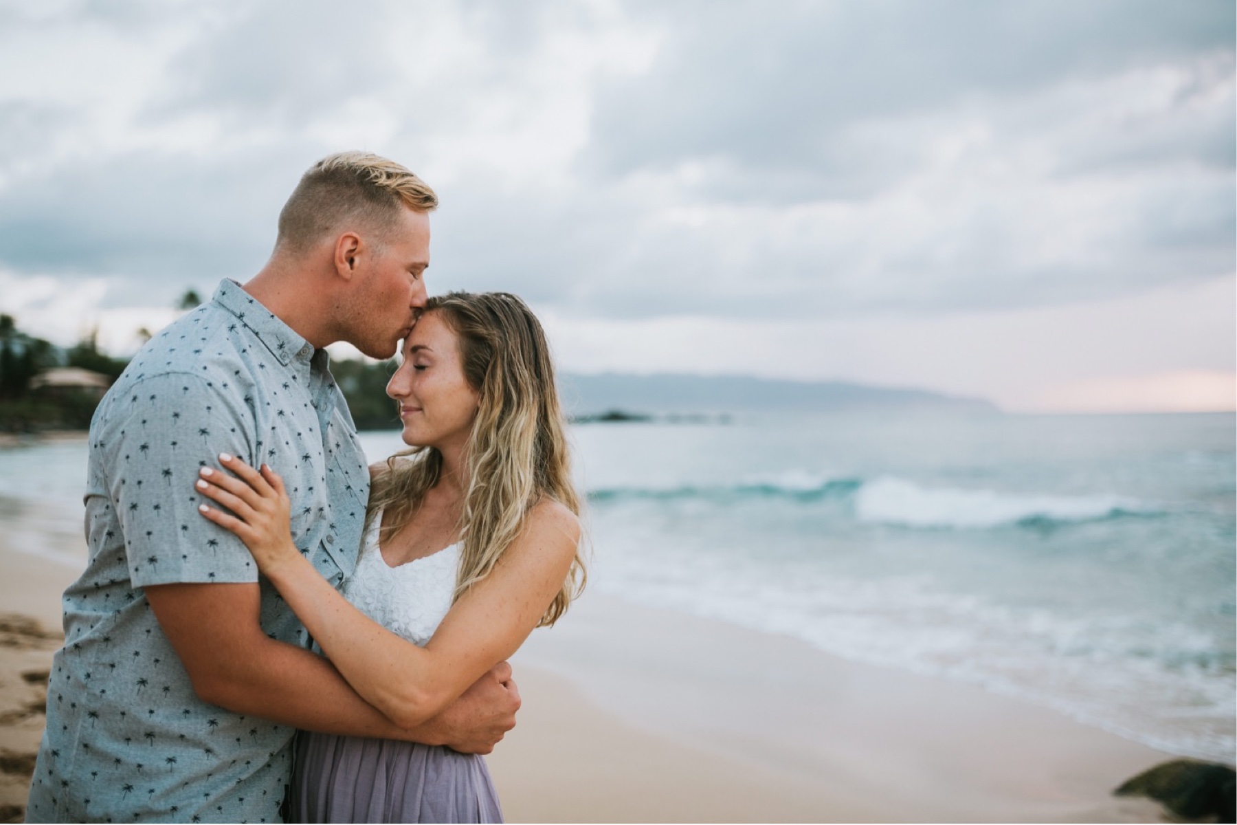 Couple standing on beach he is kissing her forehead