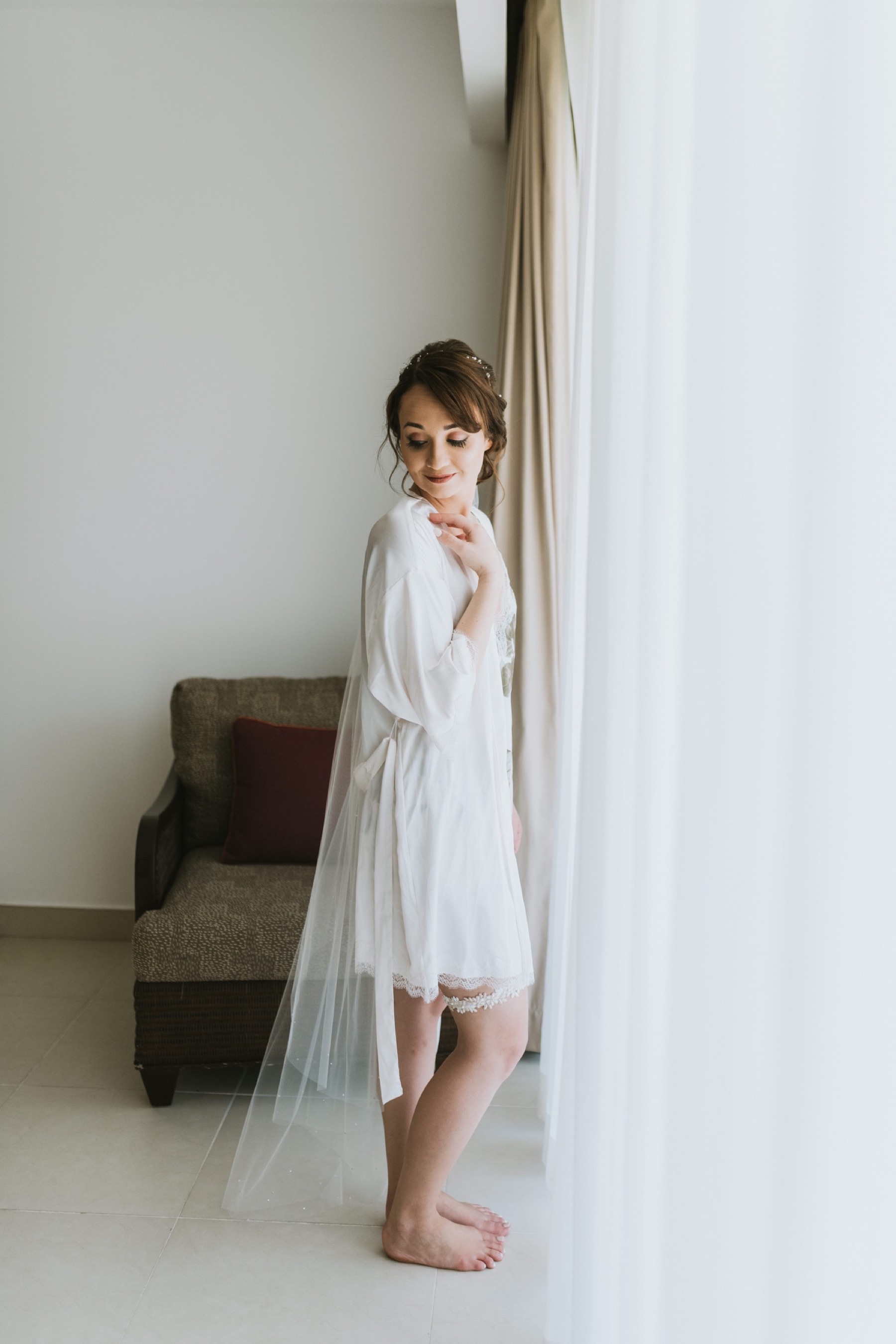 Bride standing in front of a window looking down at her shoulder with her bride robe and veil on