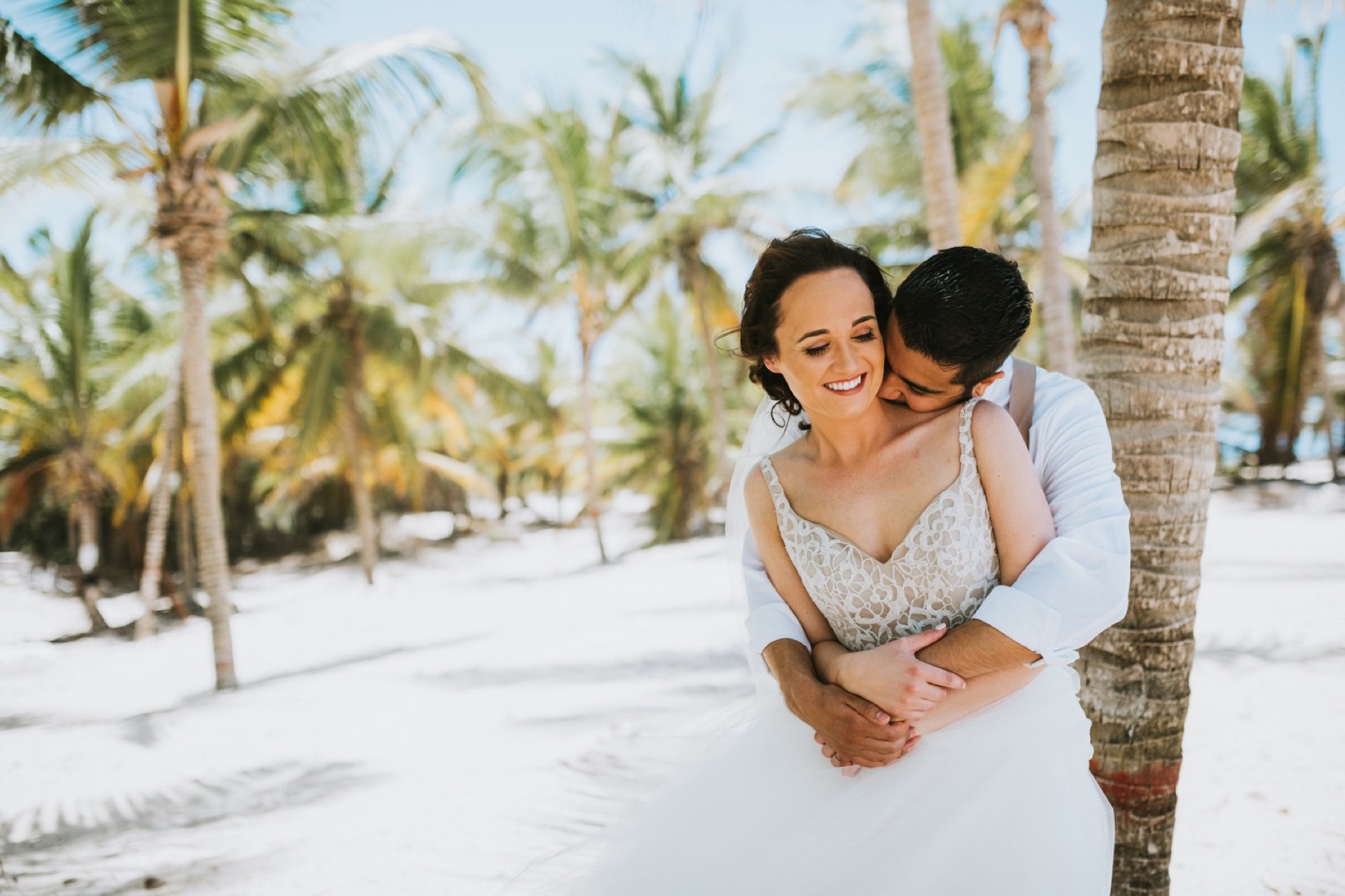 Vibrant and colorful photos of couple in palm tree grove of groom kissing brides neck