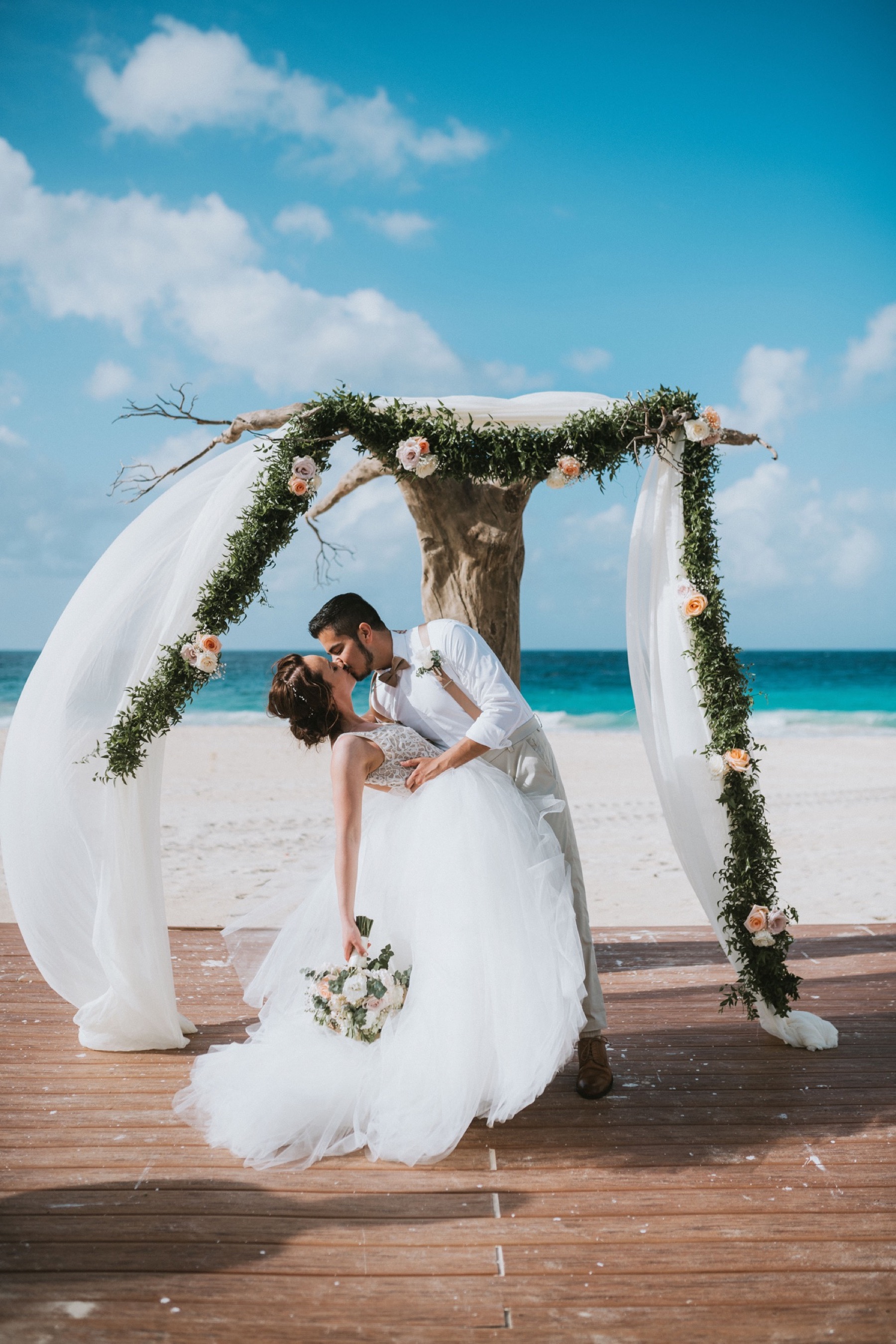 Bride and groom dip kissing in front of driftwood arch at Hard Rock Punta Cana