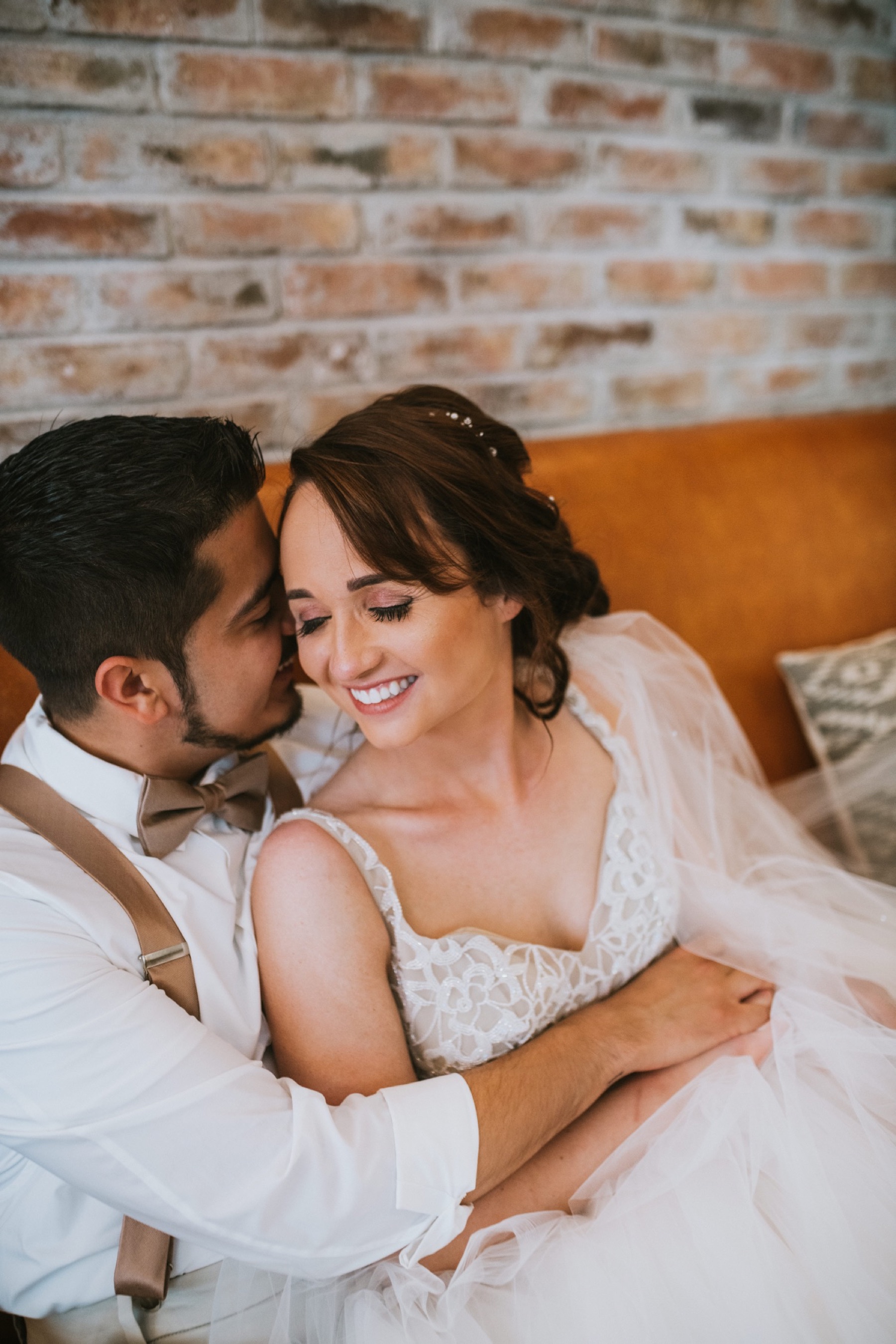 Bride and groom sitting on orange leather couch snuggling