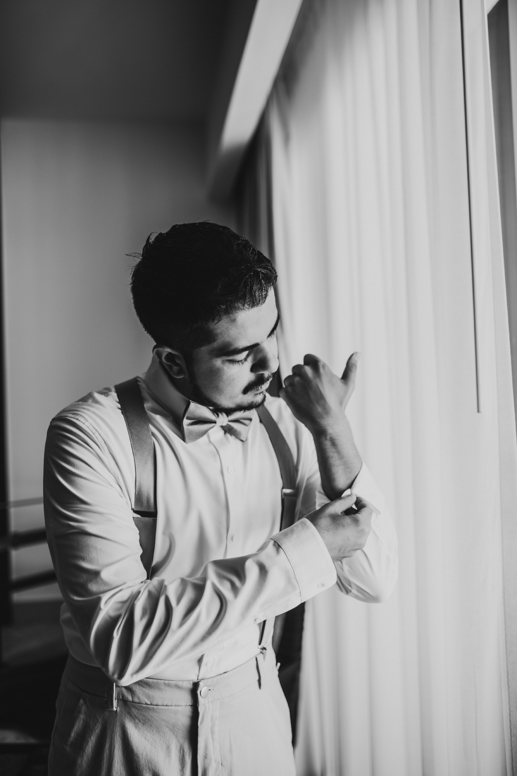 Black and white photo of a groom buttoning his sleeves on his shirt.