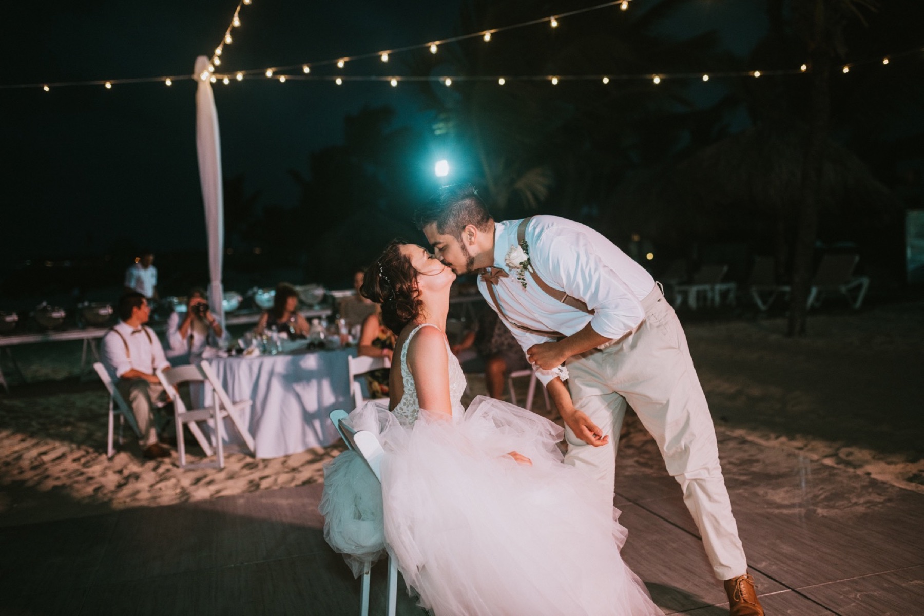 Groom kissing bride after taking garter off her at reception