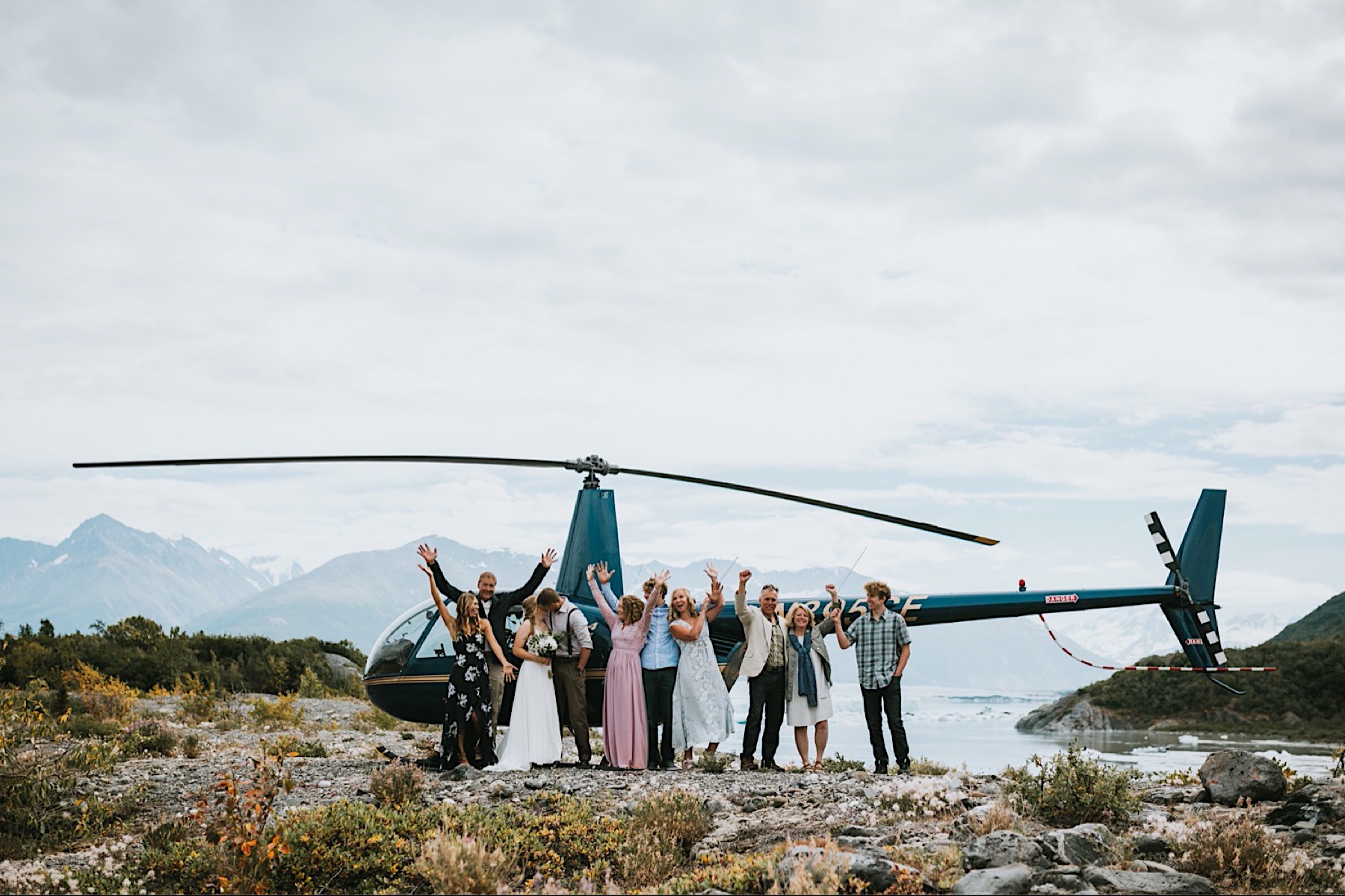 All of bride and grooms guests cheering as they kiss in front of a helicopter