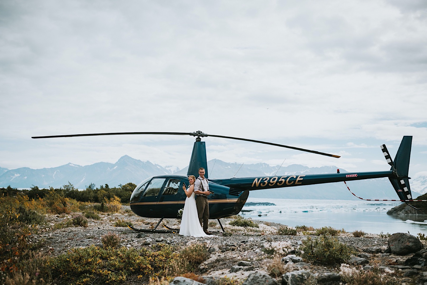 Bride and groom holding guns in front of a helicopter