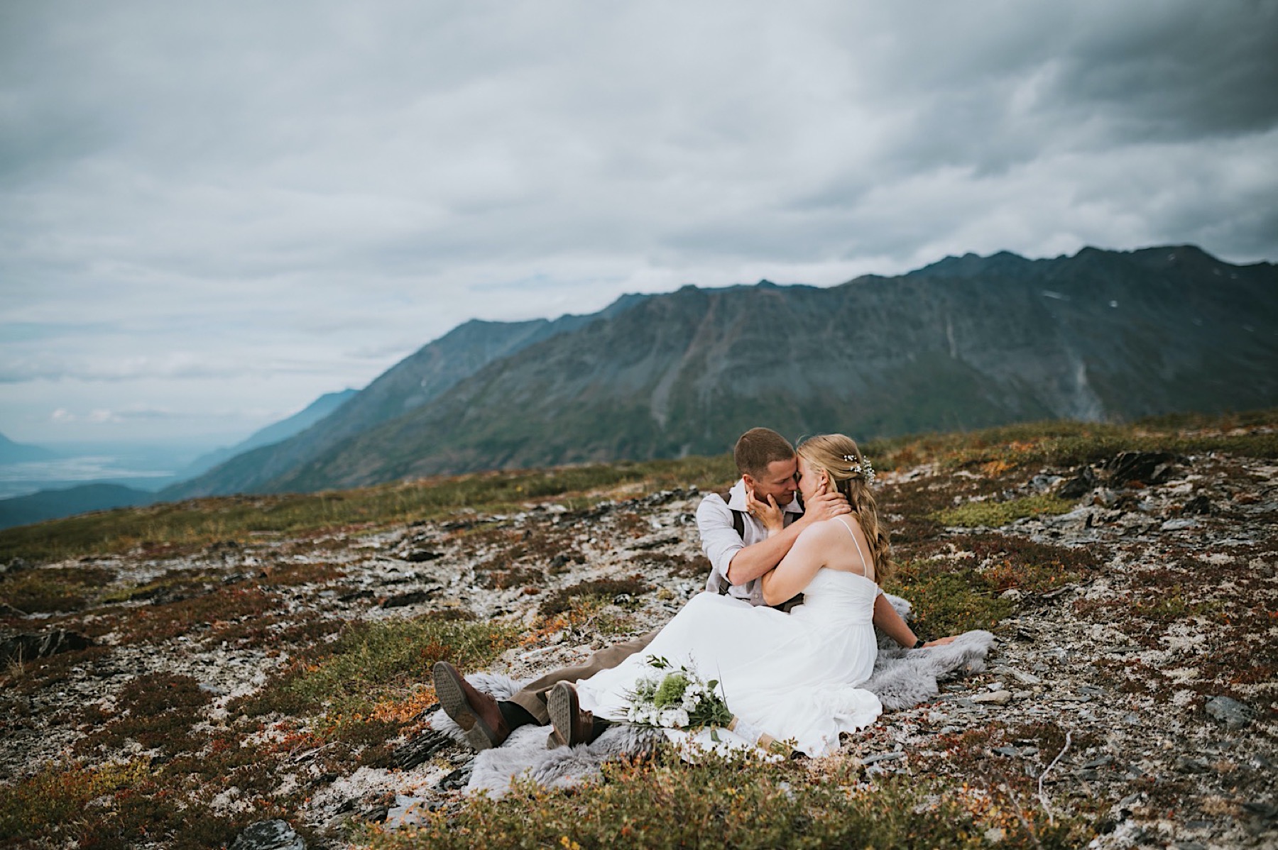 Bride and groom sitting on a mountain top during their alaska destination wedding