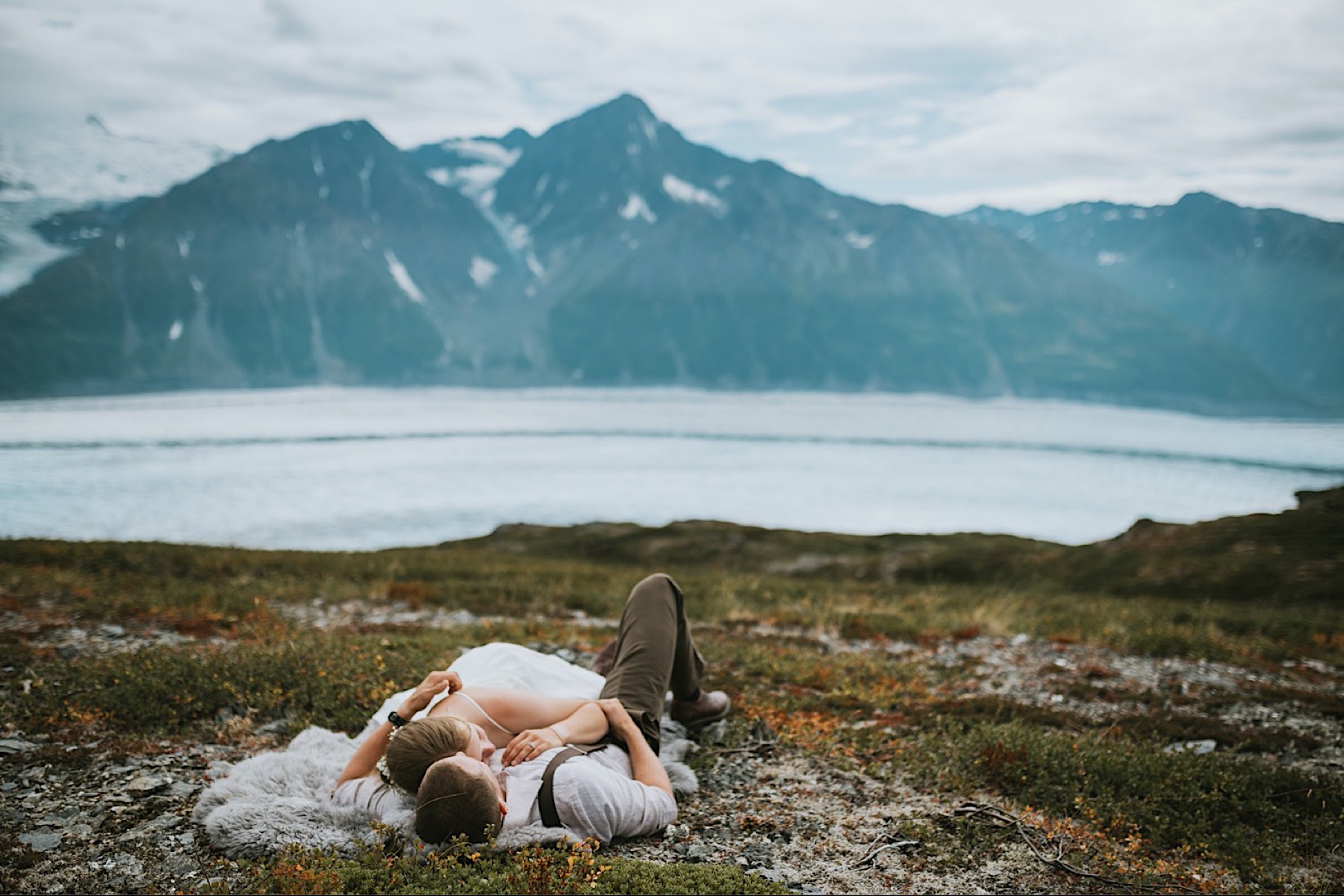 Bride and groom laying in the moss on a fur rug on a mountain top during their alaska destination wedding
