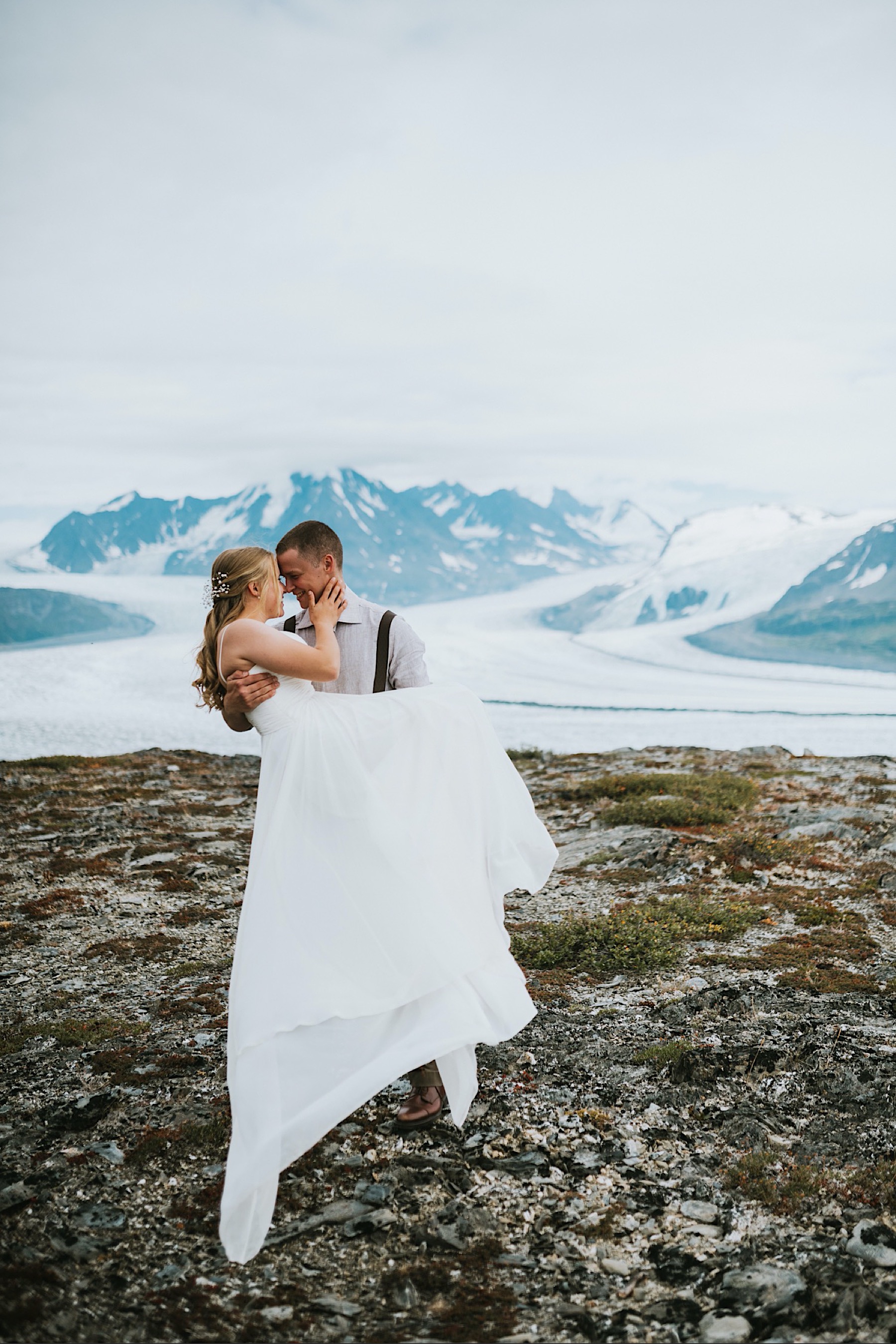 Groom picking his bride up in front of knik glacier during alaska destination wedding