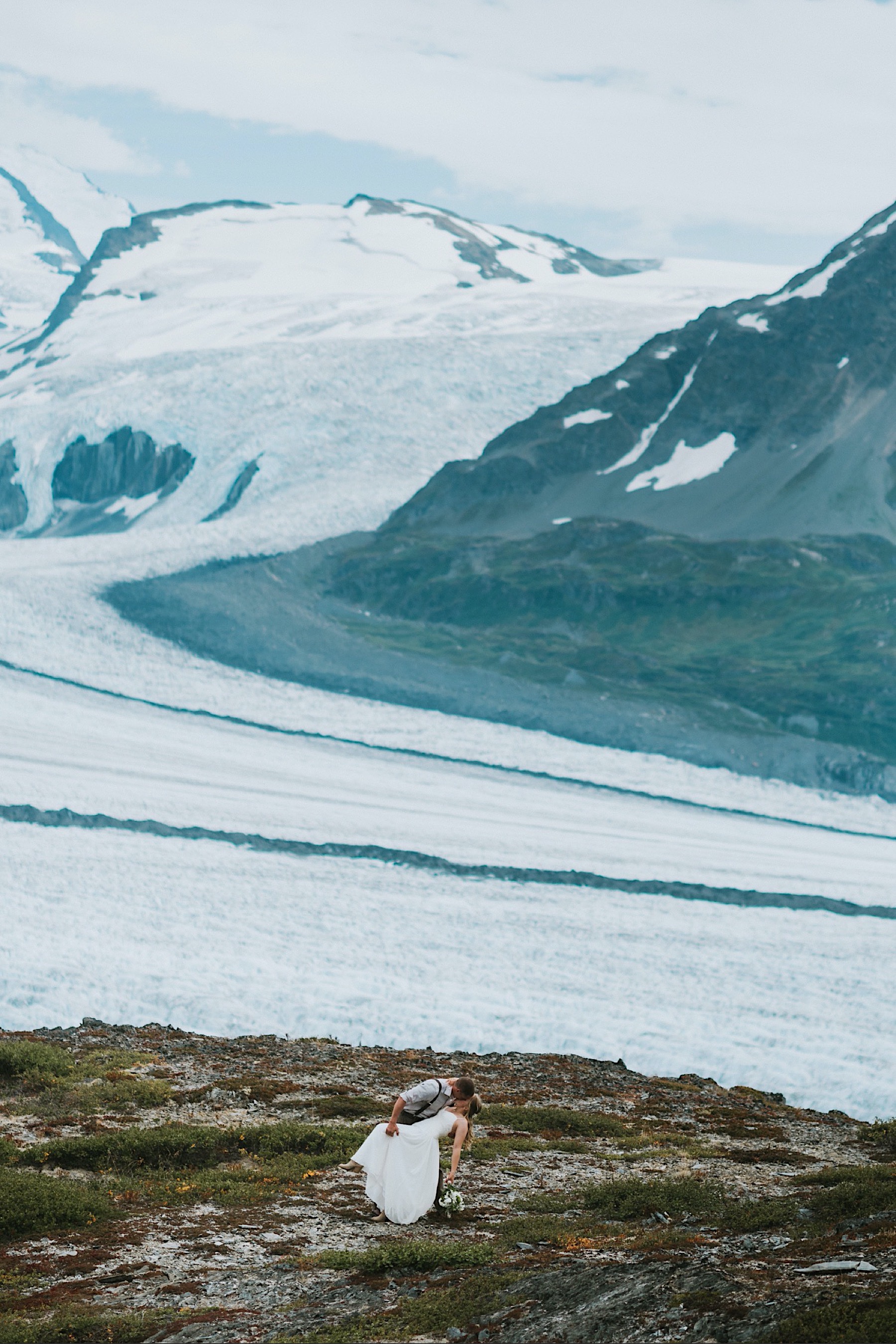 Bride and groom dip kissing on top of grasshopper ridge with Knik glacier in the background