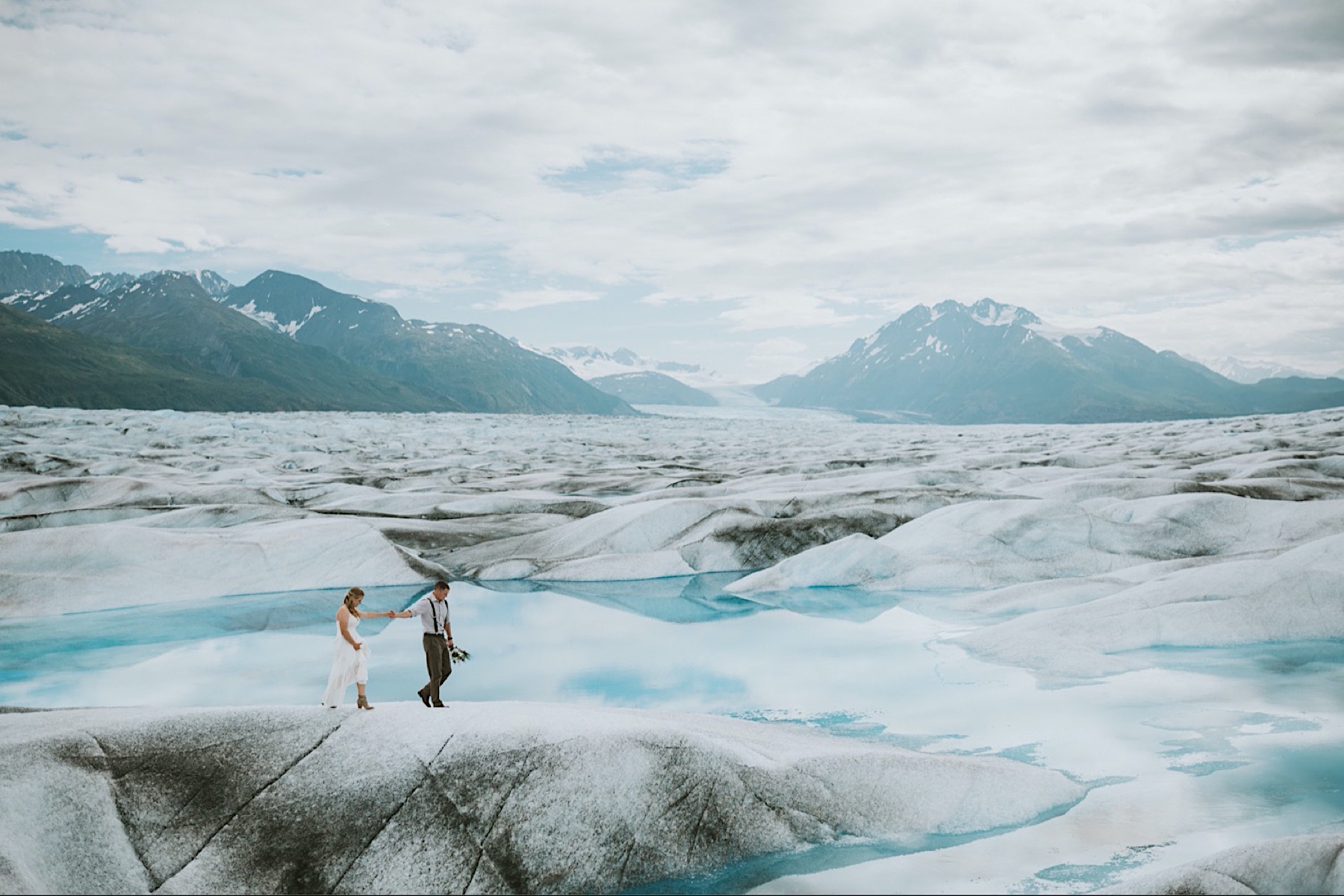 Groom leading his bride out over the blue ice of the Knik Glacier during their alaska elopement