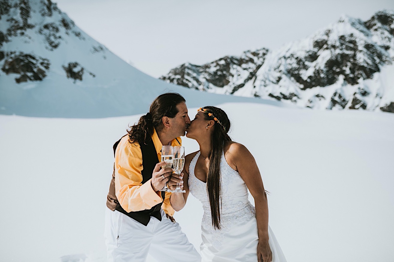 Bride and groom kissing and cheersing their champagne after their glacier elopement