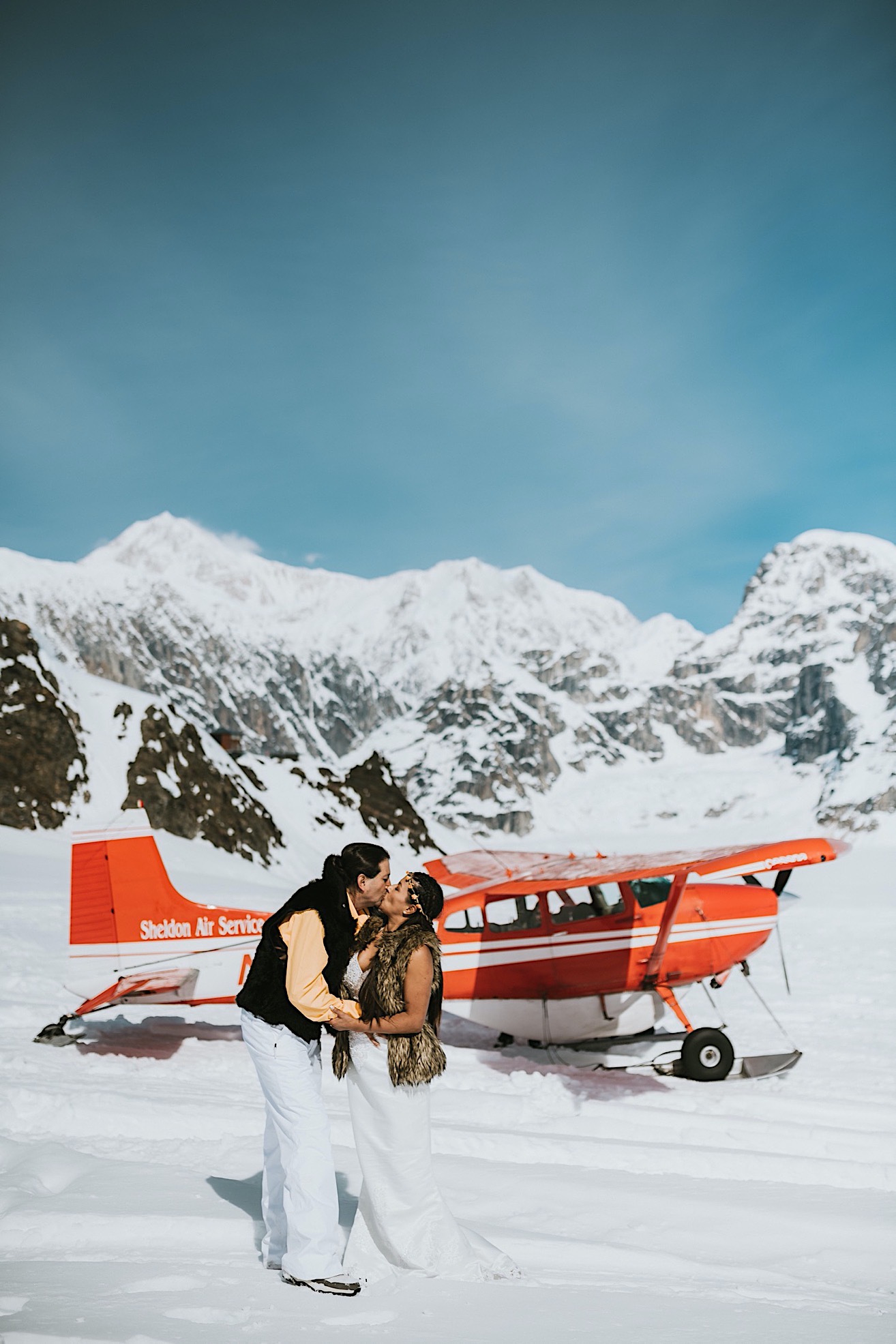 Bride and groom kissing in front of a red sheldon air services plane on ruth glacier