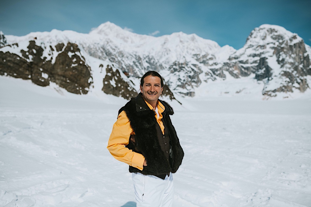 Groom wearing a yellow shirt and fur vest smiling at the camera in front of Denali