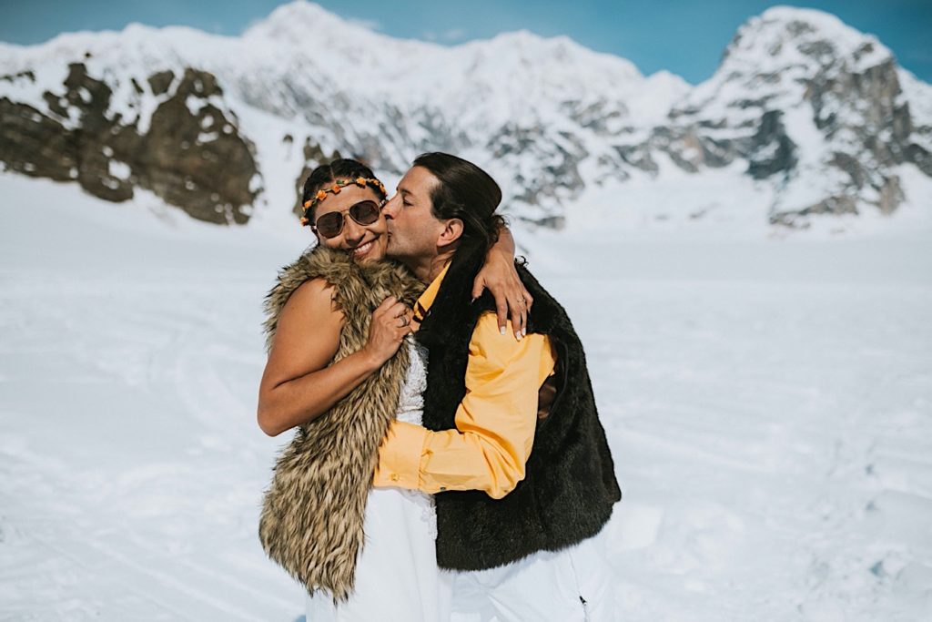 Groom hugging and kissing his brides cheek on Ruth Glacier