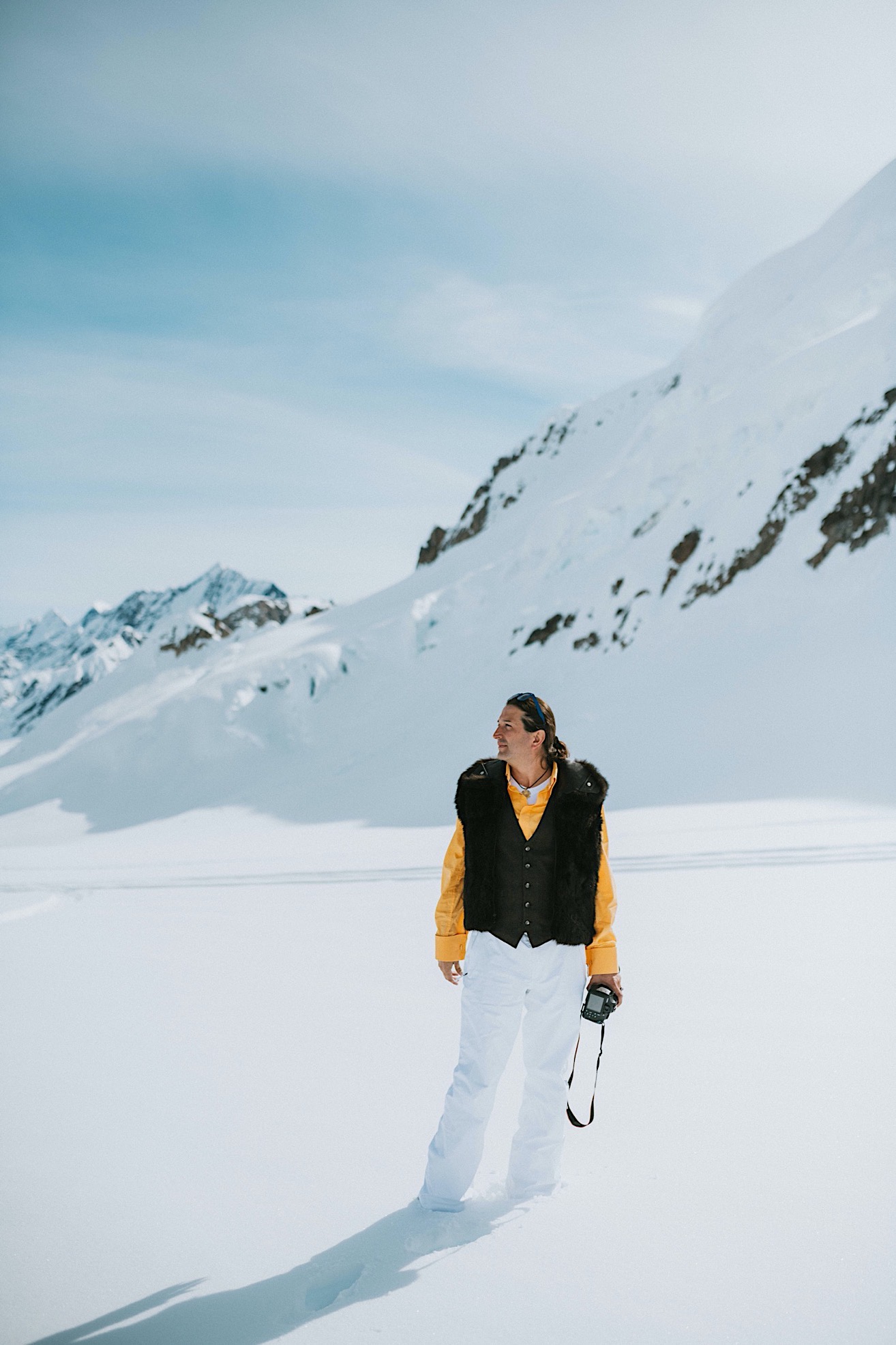Groom wearing a fur vest and snow pants on a glacier before his alaska glacier wedding
